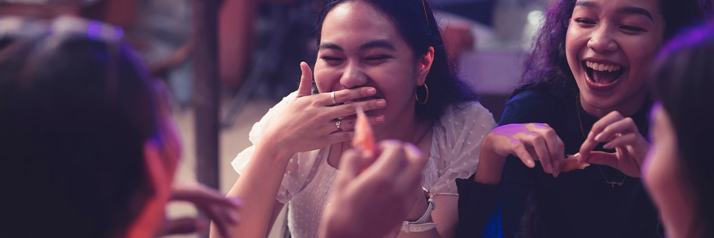 Groupe de jeunes qui rient et mangent autour d’une table au restaurant