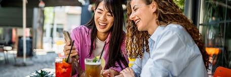 Deux jeunes femmes riant en regardant un smartphone à la terrasse d’un café