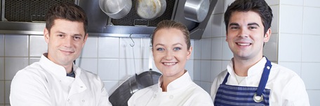 Deux cuisiniers et une cuisinière souriants dans la cuisine d'un restaurant