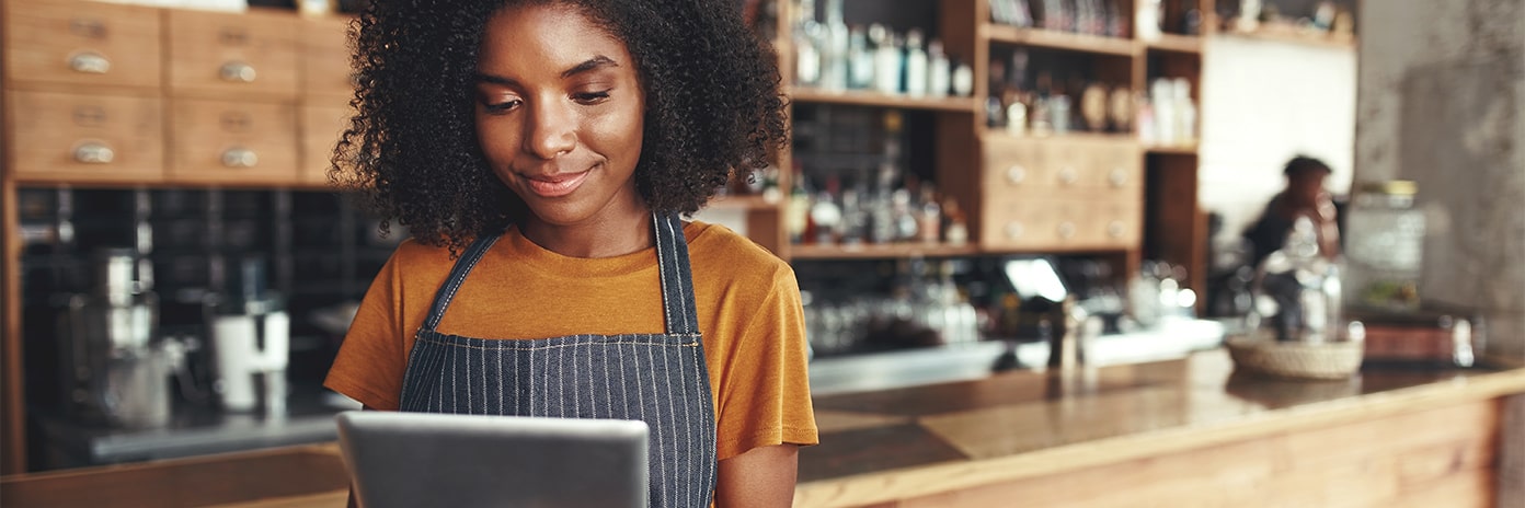 Femme avec un tablier regardant une tablette à son comptoir