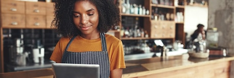 Femme avec un tablier regardant une tablette à son comptoir