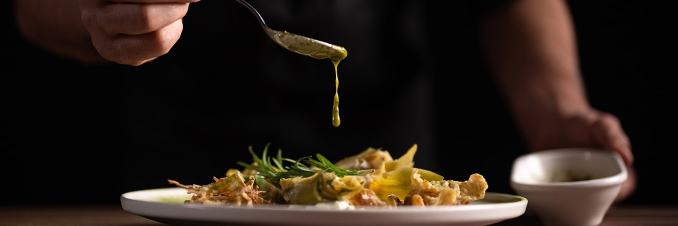 Un chef verse de la sauce sur une assiette d’artichaut