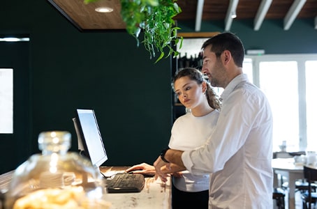 Jeune femme lors de son premier jour de travail en train d'apprendre l’encaissement, avec un collègue, dans un café