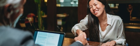 Un homme et une femme se serrent la main, tous deux assis à un bureau, après un entretien d’embauche