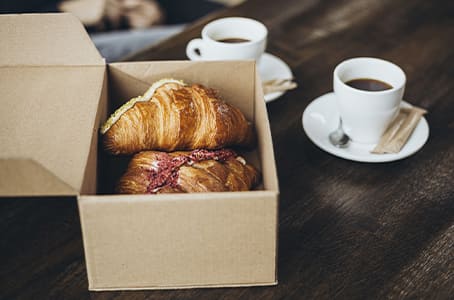 Croissant à emporter dans une boîte en carton et cafés sur une table