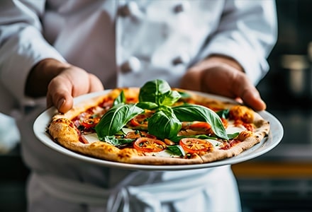 Un chef présente une pizza avec beaucoup de garnitures, dont du basilic