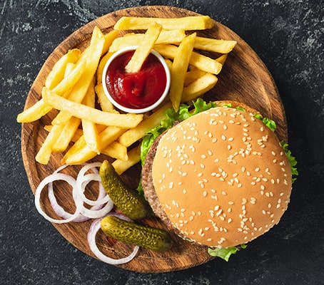 Burger avec frites, oignons, cornichons et sauce sur une assiette en bois