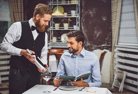 Serveur souriant présentant une bouteille de vin à un client