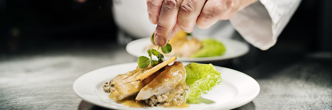 Chef cuisinier réalisant le dressage d'une assiette avec du poulet
