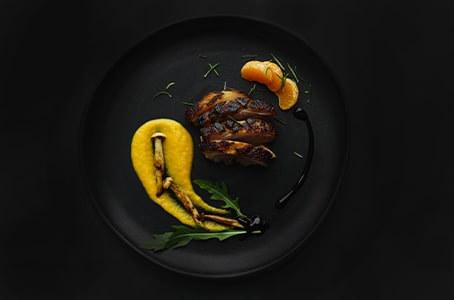 Une recette premium composée de viande blanche, champignons et mandarines, disposée dans une assiette noire