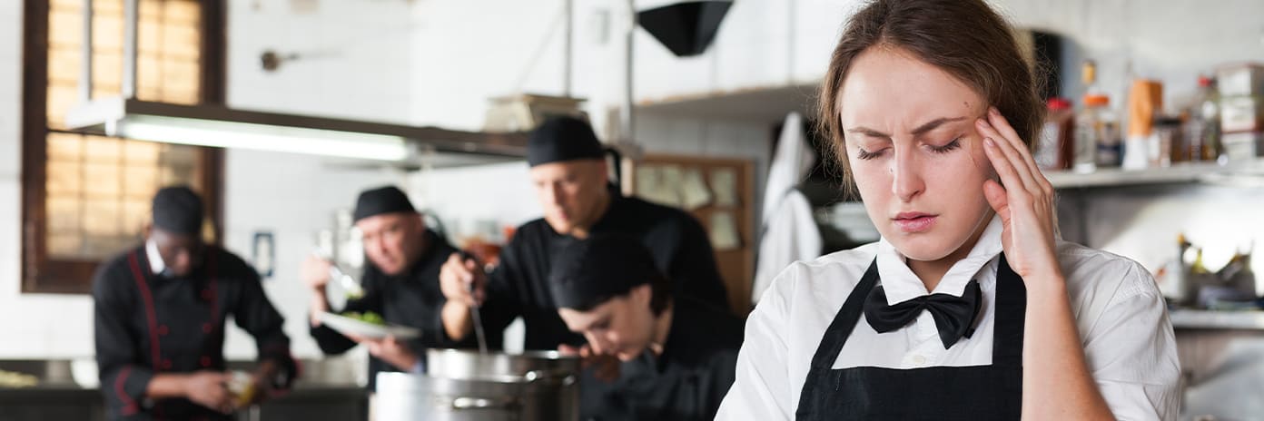 Serveuse dans une cuisine de restaurant qui se tient la tête