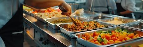 Différents plats disposés dans des bacs gris de cuisine professionnelle, prêts à être servis
