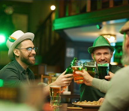 Groupe d'hommes souriants avec des chapeaux traditionnels, buvant une bière dans un pub pour la St. Patrick