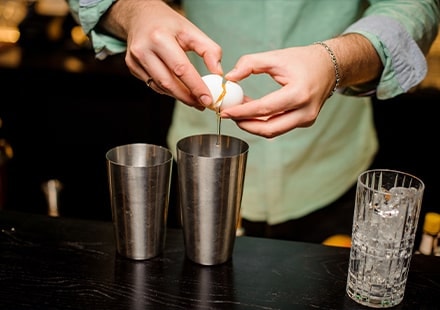 Un barman casse un œuf dans un shaker