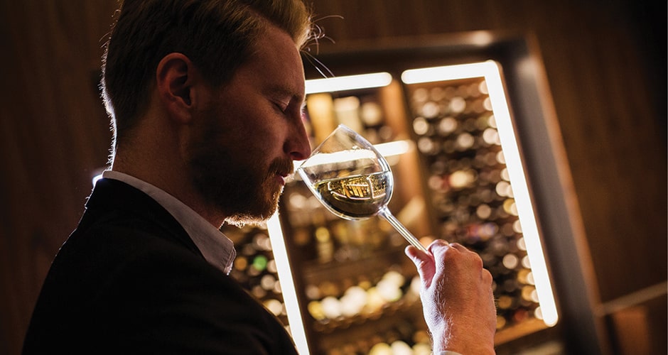 Homme dégustant un vin blanc devant une cave à vin