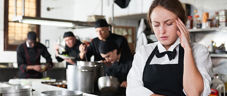 Serveuse dans une cuisine de restaurant qui se tient la tête