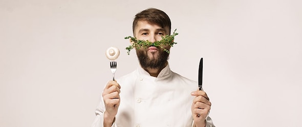 Chef de restaurant "durable" avec une fausse moustache en végétal, un couteau et une fourchette dans les mains