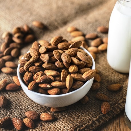 Fructe uscate - migdale in bol alb de portelan langa sticle cu lapte pe panza de sac