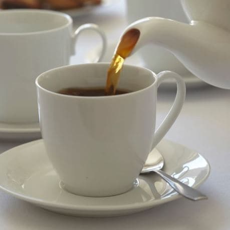 Ceai negru frunze in infuzie turnat din ceainic alb in ceasca de ceai din portelan