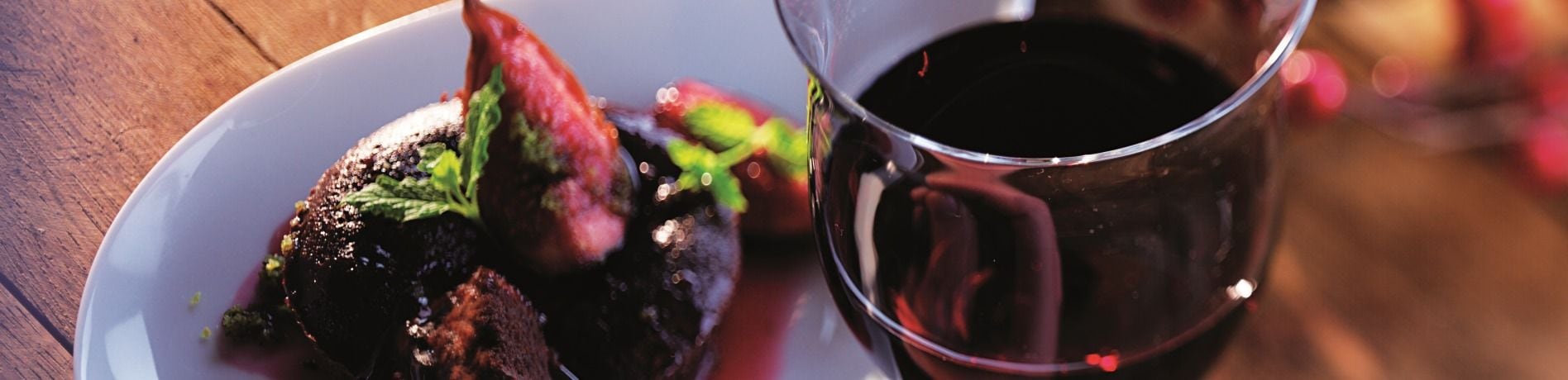 Vin rosu servit in pahar de cristal langa farfurie cu mancare
