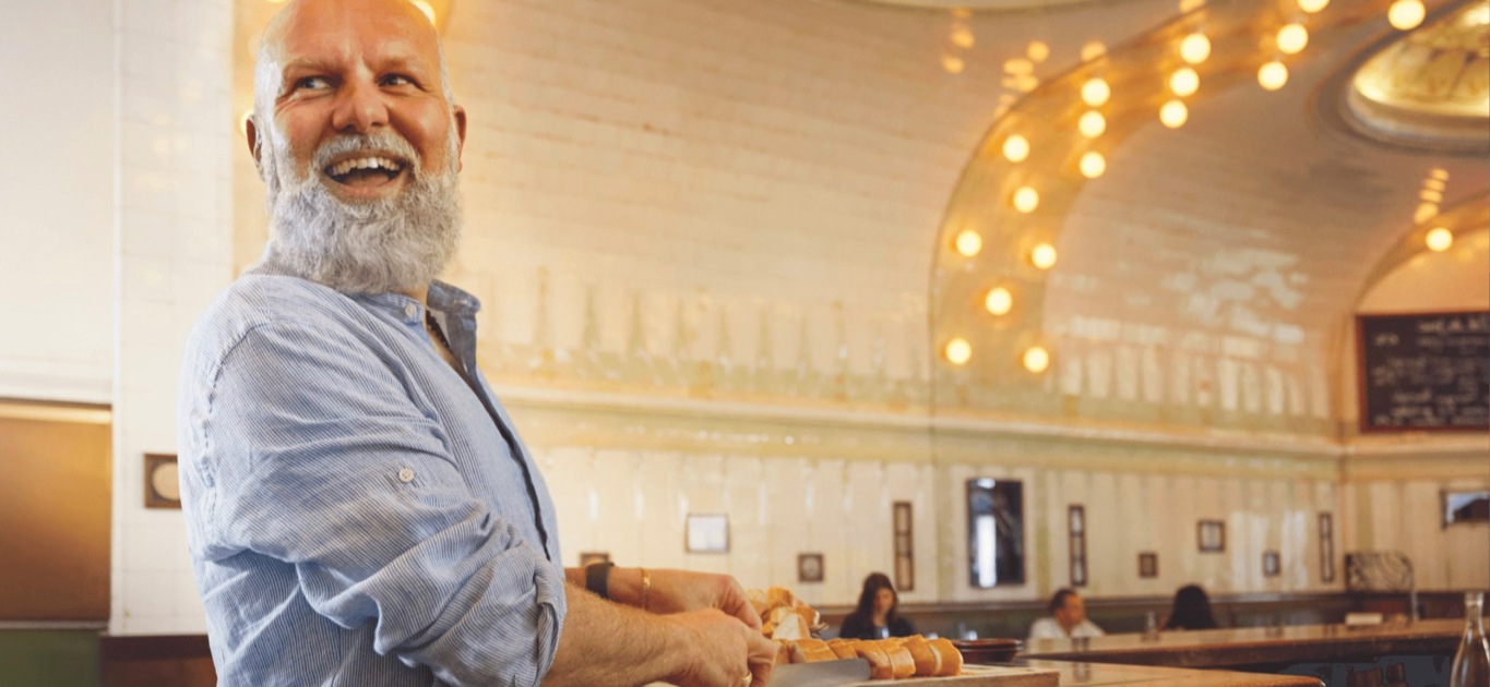 Homem com barba a cortar pão na bancada