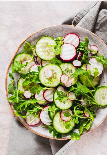 Salată proaspătă cu felii de castravete, ridichi și frunze de rucola, preparat ușor și sănătos.