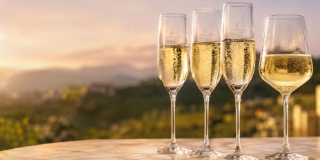 Pahare elegante de Prosecco și un pahar tip lalea cu vin spumant auriu, așezate pe o masă de marmură, în lumină caldă de apus, cu dealuri verzi estompate în fundal.
