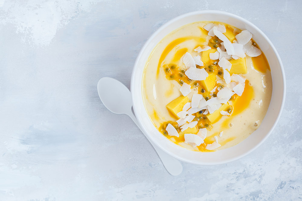 Біла миска з тропічним смузі-боулом, прикрашена кокосовою стружкою, манго та маракуєю.