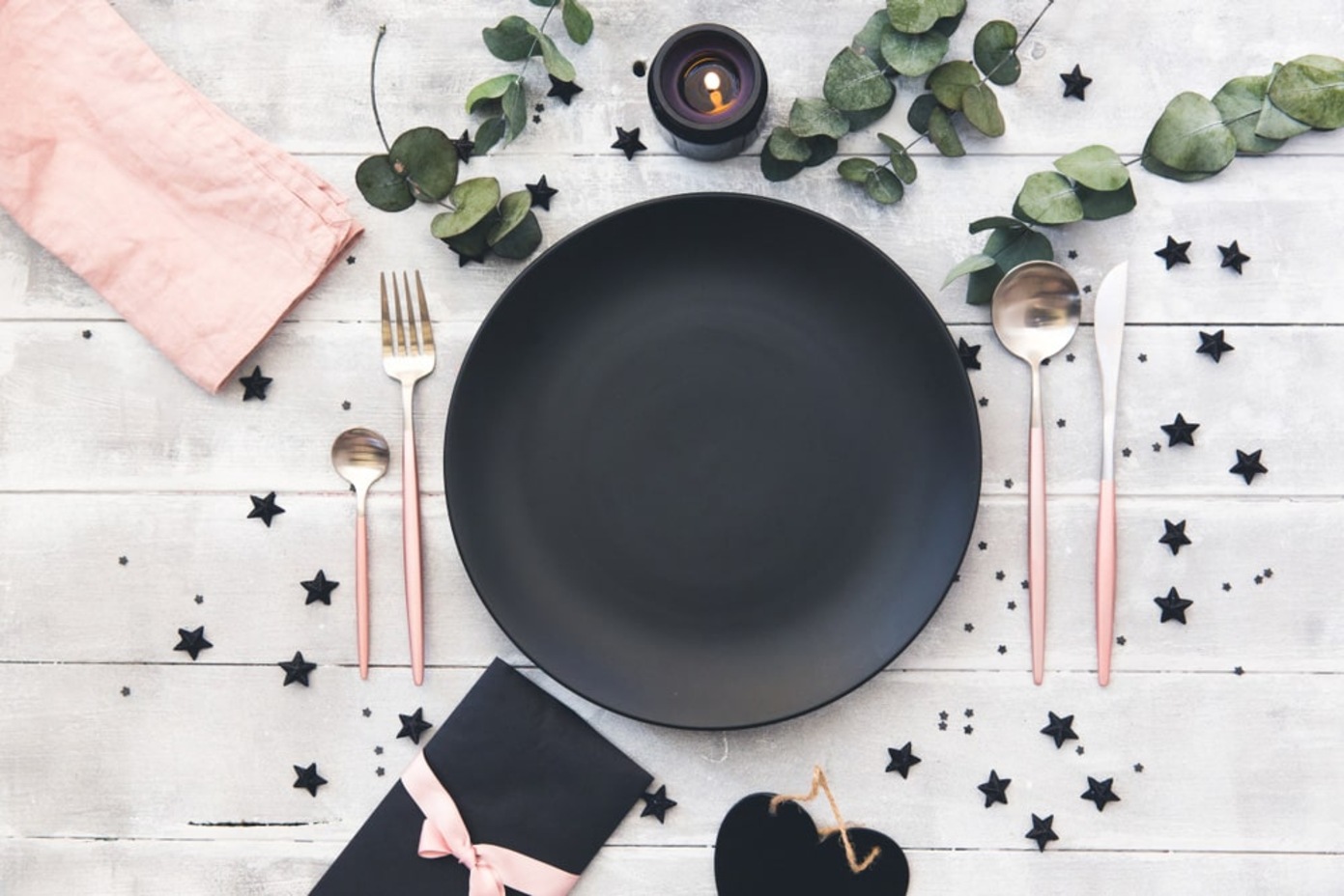 Чорна тарілка та рожеві прибори на святковому столі з декором з листя та зірочок.