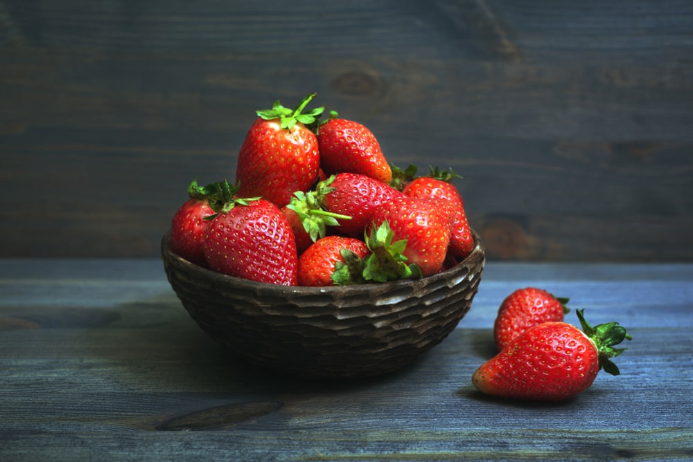 Свіжа полуниця в плетеній мисці на темному дерев’яному тлі.