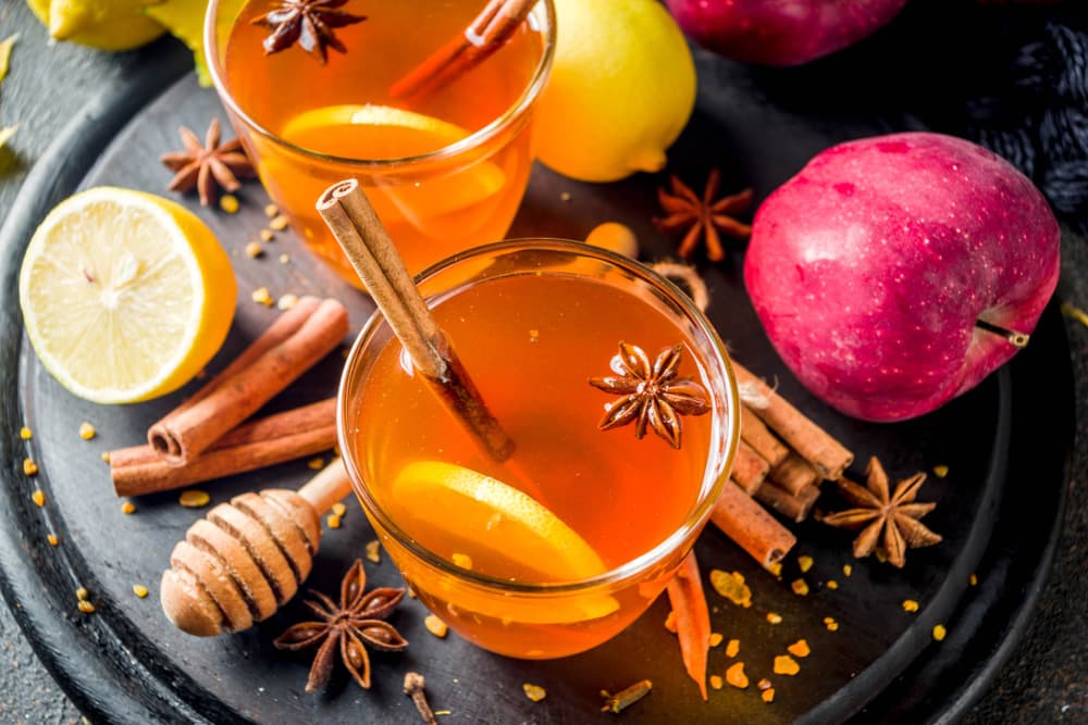 Гарячий яблучний напій з медом, корицею, лимоном та бадьяном у склянці на чорній тарілці