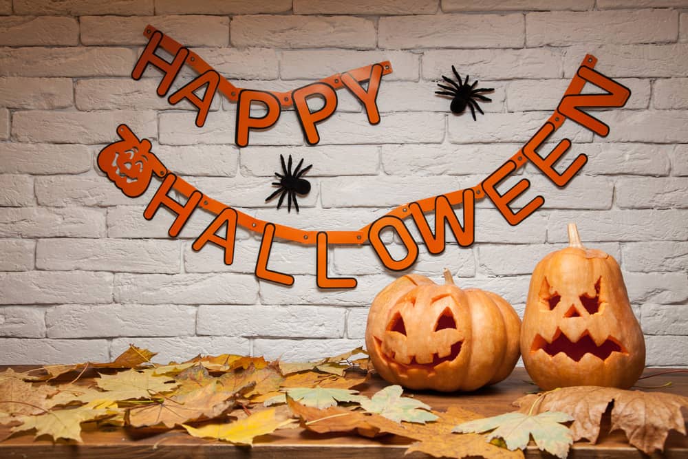 Гірлянда з написом "Happy Halloween", гарбузи зі свічками та осіннє листя на дерев'яному столі.