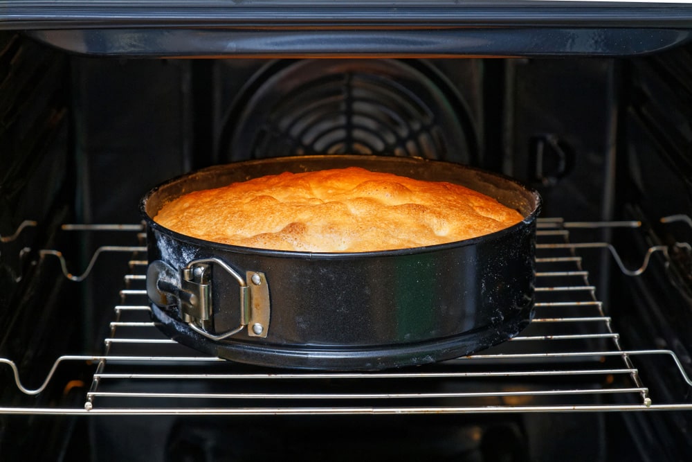 Квадратна яблучна шарлотка з рум’яною скоринкою, поруч червоні яблука і палички кориці