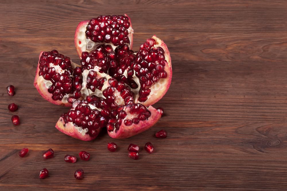 Розсипані зерна граната і шматочки фрукта на дерев’яній поверхні