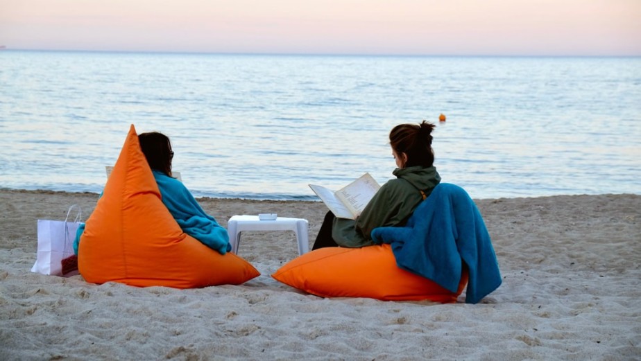 Дві жінки на помаранчевих кріслах-мішках читають біля моря на заході сонця