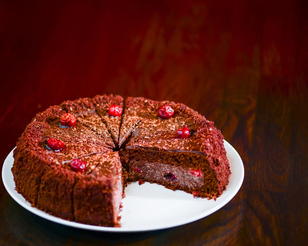 Шоколадний торт з вишнями на білому тарілці, шматок частково вийнятий