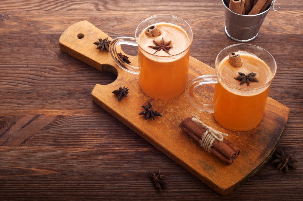 Дві склянки з гарячим яблучним сидром, корицею й бадьяном на дерев’яній дошці.