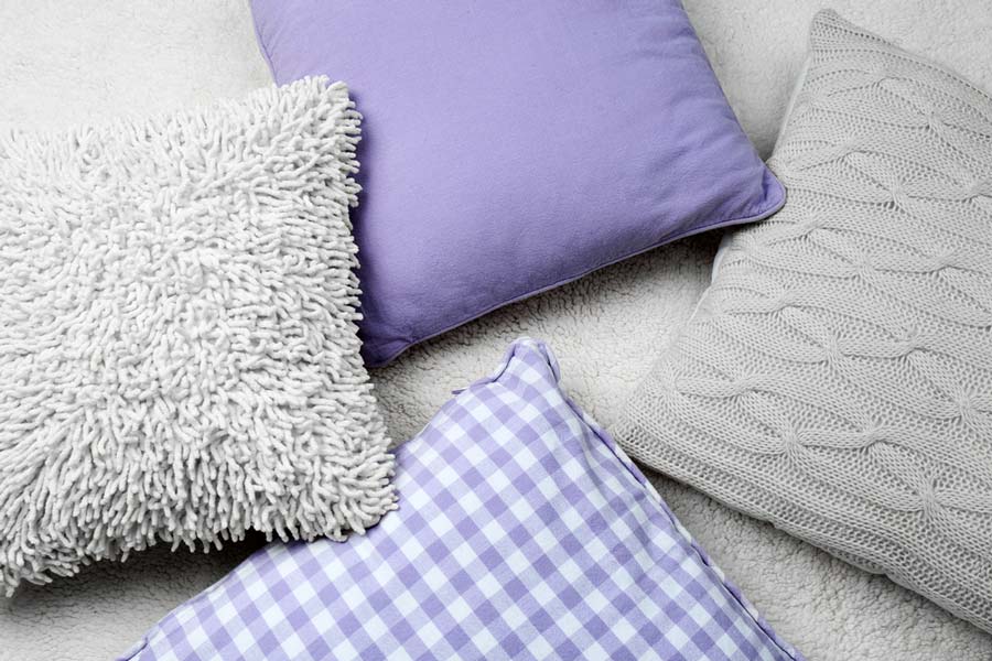 Набір різних подушок з різною текстурою і узорами на світлому фоні.