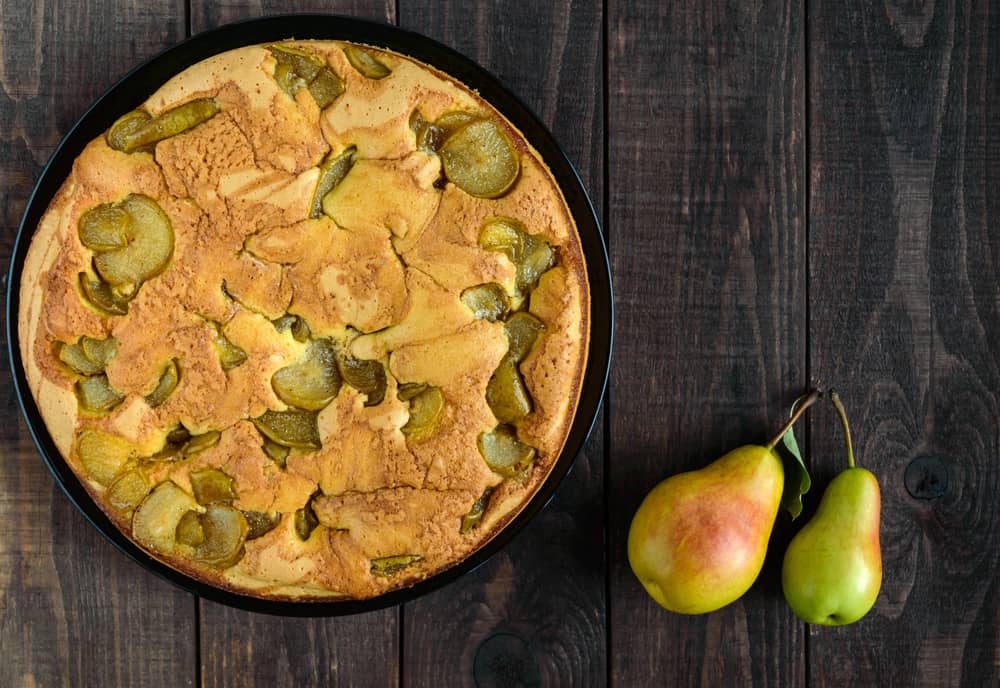 Скибка яблучної шарлотки на тарілці, прикрашена яблуками та чорницею