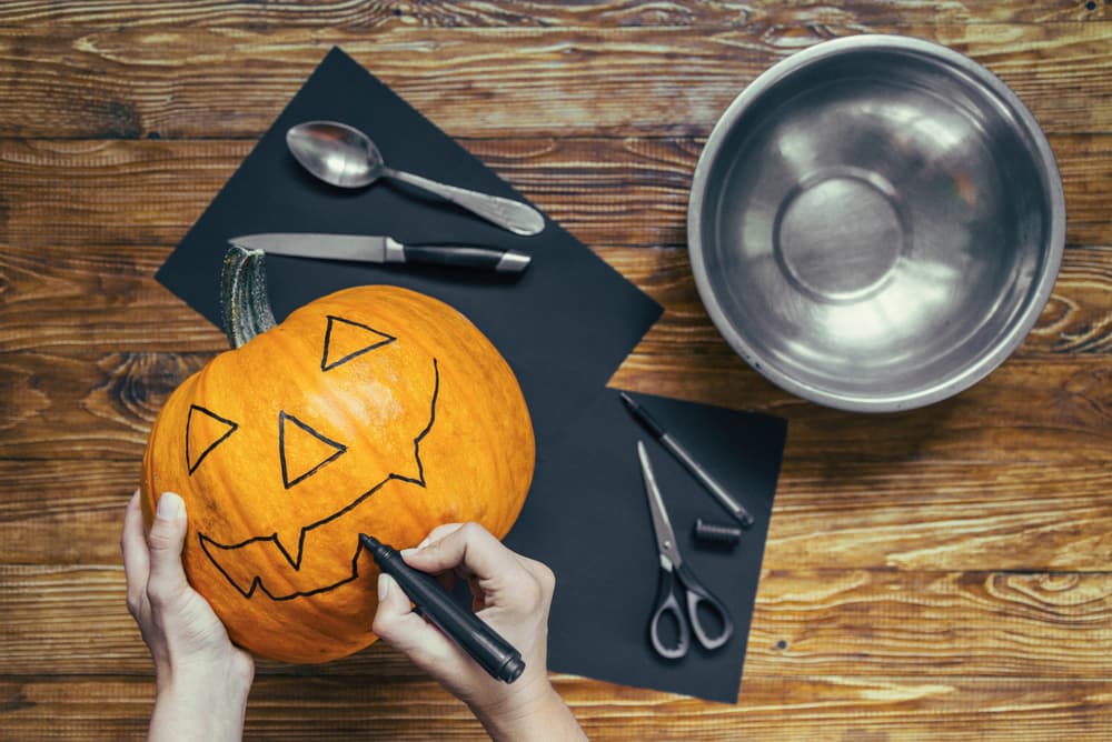 Процес малювання обличчя на гарбузі чорним маркером перед вирізанням.