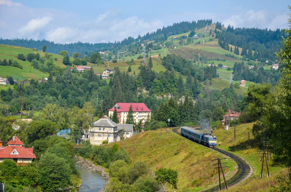 Потяг на вигнутій залізничній колії серед гірських пейзажів Карпат