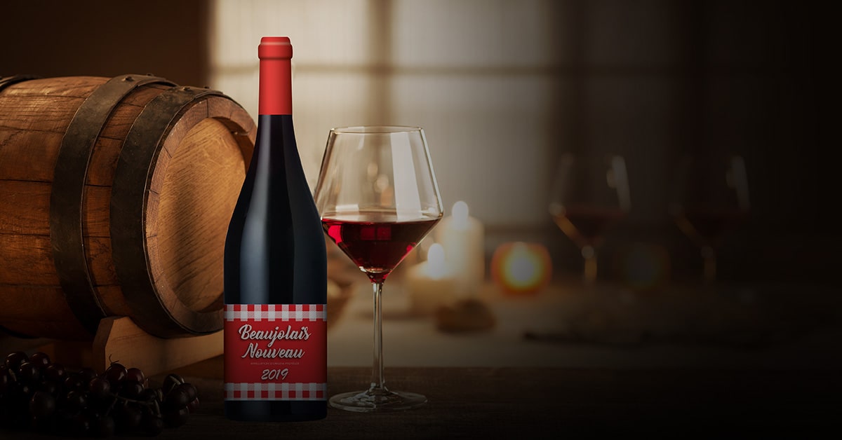 Пляшка вина Beaujolais Nouveau 2019 з келихом на фоні дерев’яної бочки та свічок.