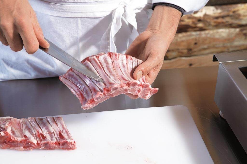 Розділювання сирих свинячих ребер ножем на кухні