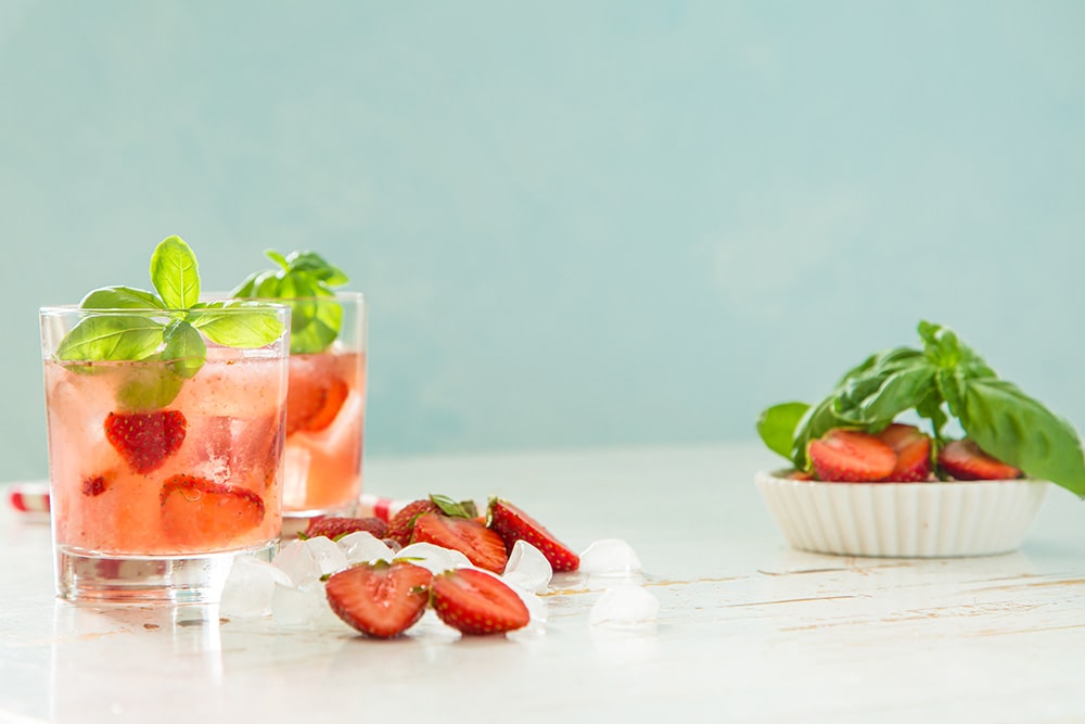 Полуничний коктейль з льодом, базиліком і свіжими ягодами у склянці на світлому фоні