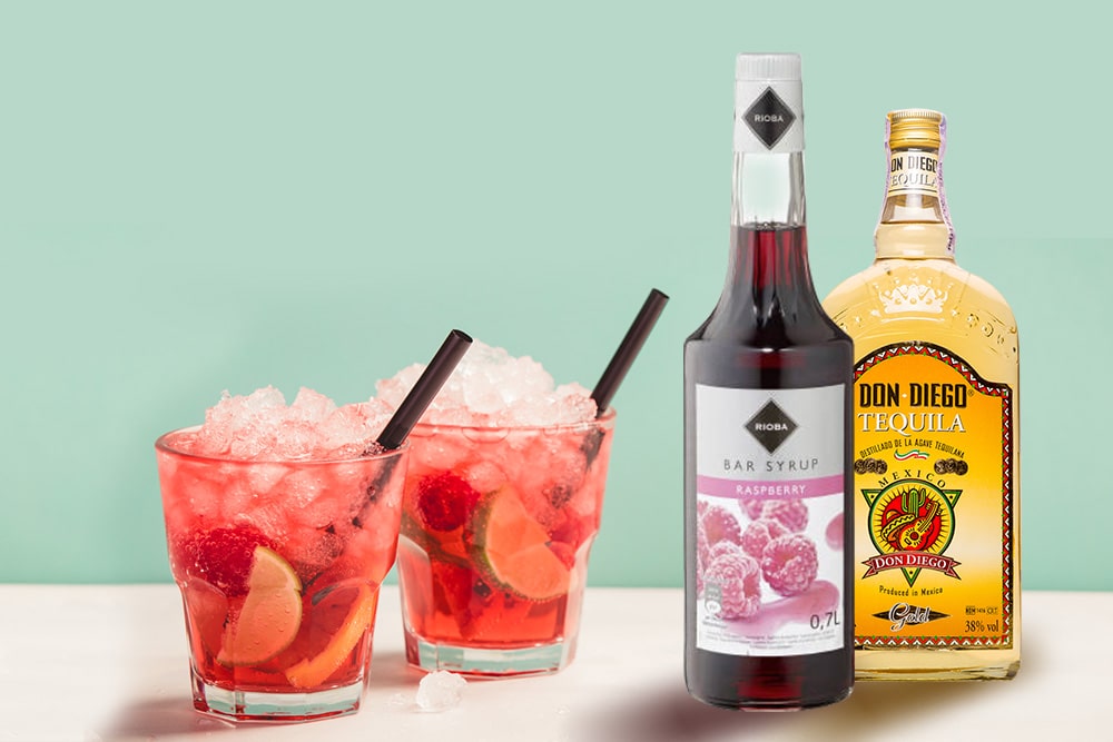 Коктейль із льодом, малиною, лаймом, пляшками текіли та малинового сиропу на фоні м'ятного кольору