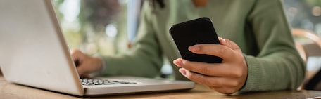 Жінка працює за ноутбуком і тримає смартфон у руці