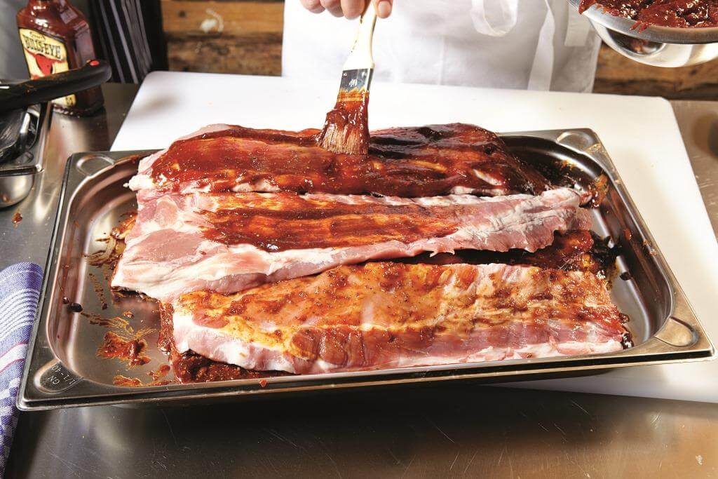 Маринування сирих свинячих ребер соусом на металевому підносі