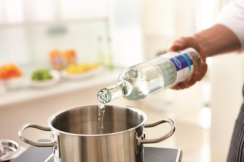 Наливання прозорої рідини з пляшки в каструлю