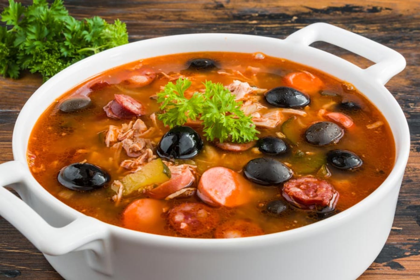Апетитна солянка з маслинами, ковбасками та зеленню в білій каструлі