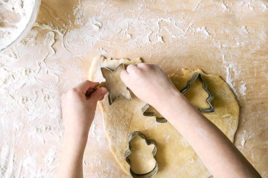 Дитина вирізає формочками новорічне печиво з тіста на присипаному борошном столі